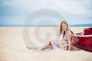 A young girl sits on the beach leaning against a boat