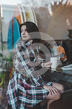 A young girl sits on a chair in a coffee shop and looks at the street through the window of the cafe