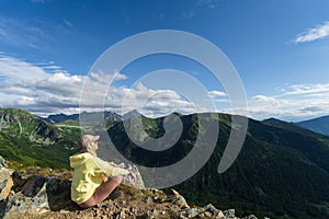 A young girl sits on a cliff in the Tatra mountains on a summer day