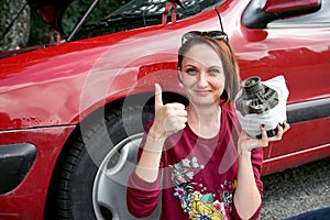 A young girl sits near a broken car and makes repairs to the electric generator, fixed it with a bandage and shows a successful ge