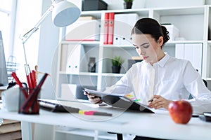 A young girl sits in the office, holds a pen in her hand and looks through documents.