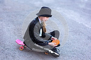 A young girl sits on a skateboard in the street and plays a new fidget toy, popular with children, and helps them to concentrate.
