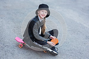 A young girl sits on a skateboard in the street and plays a new fidget toy, popular with children, and helps them to concentrate.