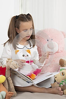 Young girl sits on the sofa at home and reads a book to her soft toys