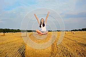 A young girl sits on a stack of straw with her hands up. Freedom, romance