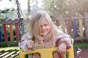 A young girl sits on a swing in a retro-styled playground.