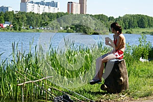 Young girl sits at water and fishes