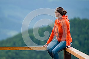 a young girl sits on a wooden handrail.