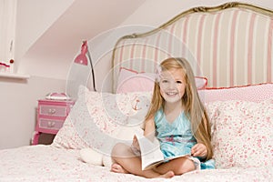 Young girl sitting on bed with book smiling photo