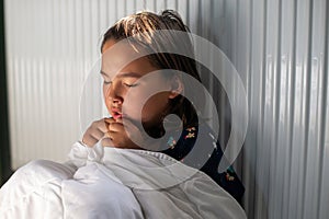 Young girl sitting with a blanket on her next to a radiator to warm herself