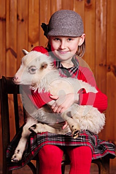 Young girl sitting on a chair, holding a lamb in his arms and looks in the picture. on the farm