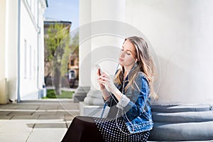 Young girl sitting on the college campus yard listening music