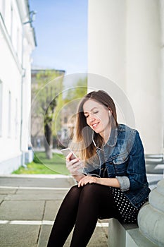 Young girl sitting on the college campus yard listening to music