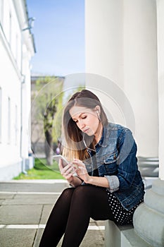 Young girl sitting on the college campus yard listening to music