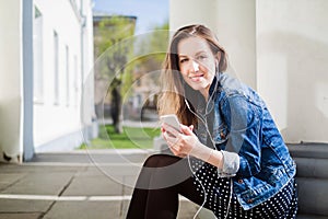 Young girl sitting on the college campus yard listening to music