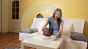 A young girl sitting on the couch pours tea from a teapot into a cup