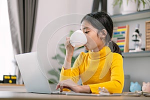 A young girl is sitting at a desk with a laptop and a cup of coffee