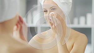 Young Girl is Sitting in front of a Make-up Mirror in the Bathroom and Applying a Skin Cream. Beautiful Woman is Making