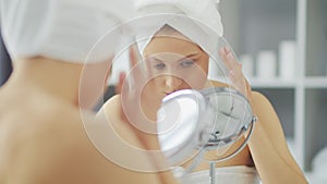 Young Girl is Sitting in front of a Make-up Mirror in the Bathroom and Applying a Skin Cream. Beautiful Woman is Making