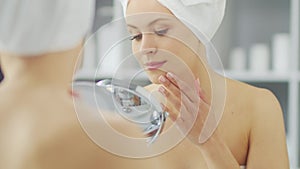 Young Girl is Sitting in front of a Make-up Mirror in the Bathroom and Applying a Skin Cream. Beautiful Woman is Making