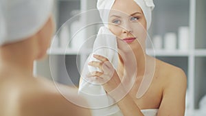 Young Girl is Sitting in front of a Make-up Mirror in the Bathroom and Applying a Skin Cream. Beautiful Woman is Making