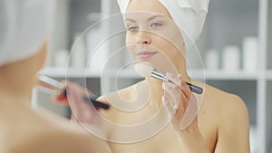 Young Girl is Sitting in front of a Make-up Mirror in the Bathroom and Applying a Skin Cream. Beautiful Woman is Making