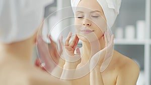 Young Girl is Sitting in front of a Make-up Mirror in the Bathroom and Applying a Skin Cream. Beautiful Woman is Making