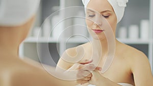 Young Girl is Sitting in front of a Make-up Mirror in the Bathroom and Applying a Skin Cream. Beautiful Woman is Making