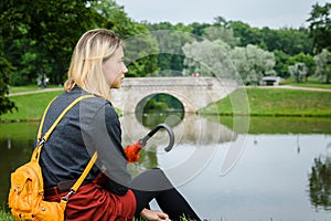 Young girl sitting on the grass in the Park by the lake with a red umbrella