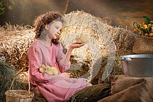 young girl is sitting in a hay bale with two baby ducks in her hands