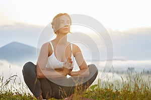 Young girl sitting in lotos pose in mountains.