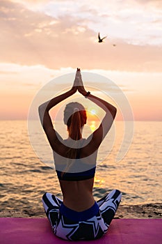 Young girl sitting in lotus position on sunrise, near the sea