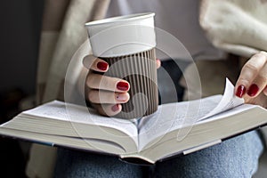 Young girl is sitting near the window, covered with a blanket, she is reading a book and drinking tea, close-up