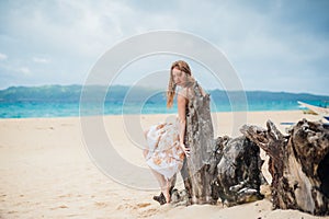 Young girl sitting on an old tree on the beach of Boracay