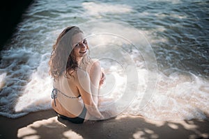 Young girl sitting in the shade of a tree in the sea waves on the coast