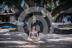 Young girl sitting in the shade of a tree in the sea waves on the coast of a tropical island