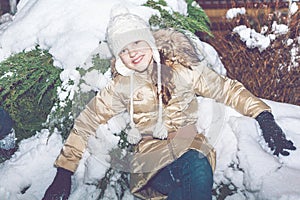 Young girl sitting on snow in evening winter forest