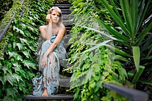 Young girl sitting on the stairs in a garden covered with ivy