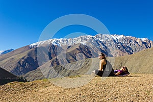Young girl sitting staring at the sun by Andes snowy mountain range