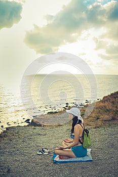 Young girl is sitting on a stony sea coast and looking at sea at sunset. Rear View.