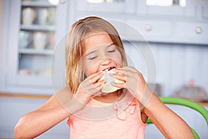 Young Girl Sitting At Table Eating Sugary Iced Bun photo