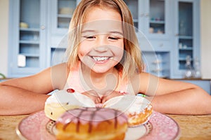 Young Girl Sitting At Table Looking At Plate Of Sugary Cakes