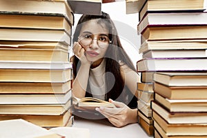 A young girl is sitting at a table with a pile of books. Sad brunette with glasses. Training and education. Close-up