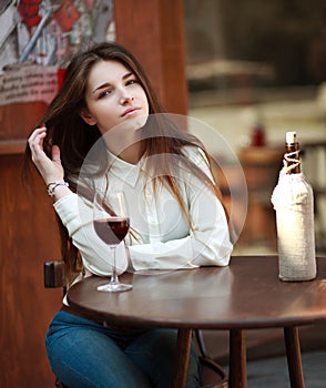 Young girl sitting at table in summer cafe with glass of wine