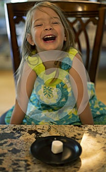 Young girl sitting at a table waiting patiently for a marshmallow