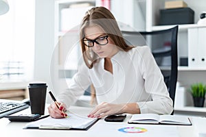 Young girl sitting at the table and working with a computer, documents and calculator