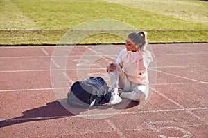 A young girl is sitting on a track and listening to the music at the stadium while preparing for a training. Sport, athletics,