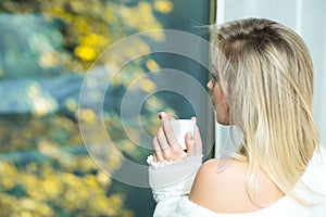 Young girl sitting at window drinking coffee and looking outside enjoys of rest. Woman drinking coffee at home with