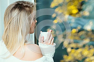 Young girl sitting at window drinking coffee and looking outside enjoys of rest. Woman drinking coffee at home with