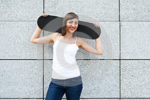 Young girl with skateboard on her shoulders in the city by the w